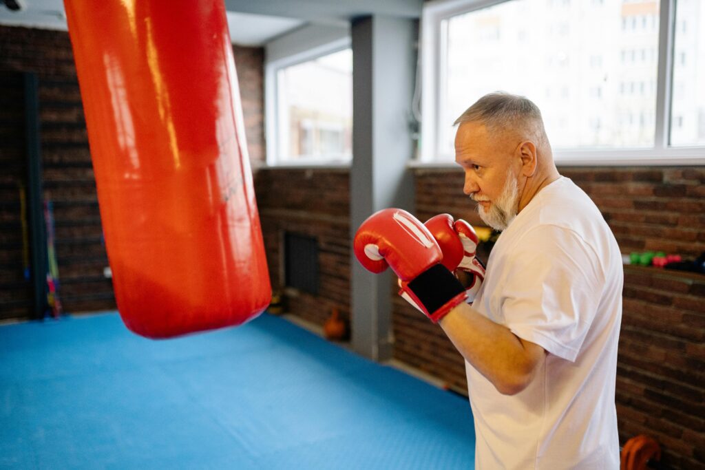 Elderly man exercising with punching bag in indoor boxing gym for fitness.