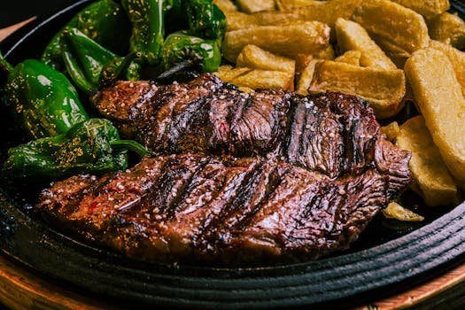 Juicy grilled beef steak with green peppers and crispy potatoes on a plate.