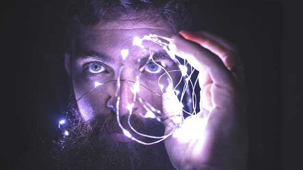 Close-up of a man with a beard holding glowing string lights, creating a mystical atmosphere.