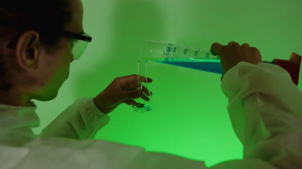 Scientist carefully pouring blue liquid into a test tube under green light.